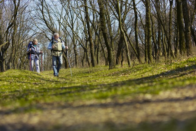 Best place in the world. Aged family couple of man and woman in tourist outfit walking at green lawn near by trees in sunny day