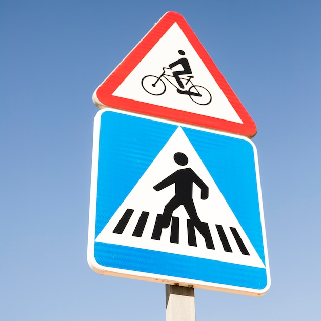 Bicycle warning sign over the modern square pedestrian crossing road sign against blue sky