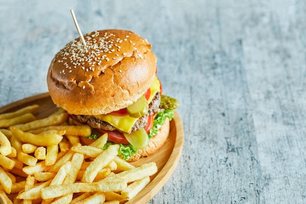 Free photo big burger with fry potato in the wooden plate on the marble table.