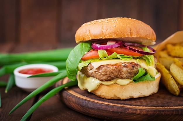 Big sandwich - hamburger with juicy beef burger, cheese, tomato,  and red onion on wooden table