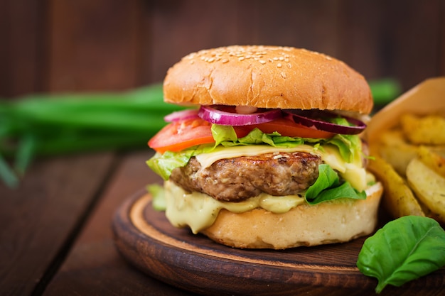 Big sandwich - hamburger with juicy beef burger, cheese, tomato,  and red onion on wooden table