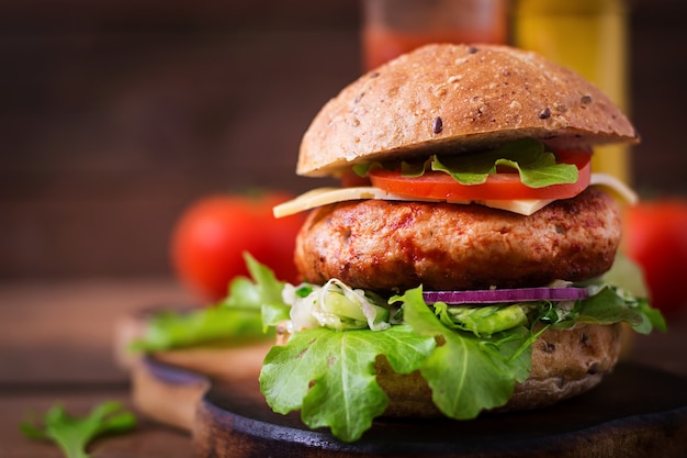 Big sandwich - hamburger with juicy chicken burger, cheese, tomato, and red onion on wooden table