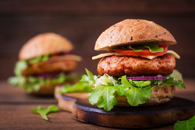 Big sandwich - hamburger with juicy chicken burger, cheese, tomato, and red onion on wooden table