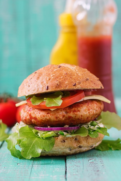 Big sandwich - hamburger with juicy chicken burger, cheese, tomato, and red onion on wooden table