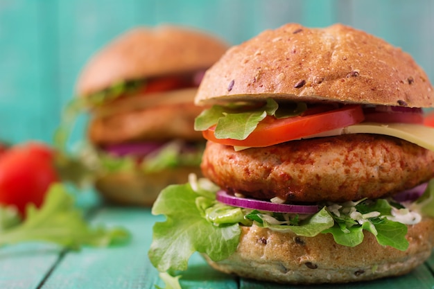 Big sandwich - hamburger with juicy chicken burger, cheese, tomato, and red onion on wooden table