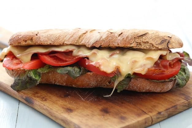 Big vegan sandwich with vegetables and cheese on wooden board table