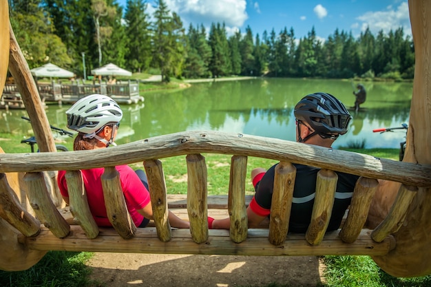 Free Photo biker couple on a tour at lake bloke resting on a wooden swing