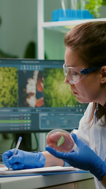 Free photo biologist woman writing medical expertise while holding petri dish with vegan beef meat in hands working in microbiology laboratory