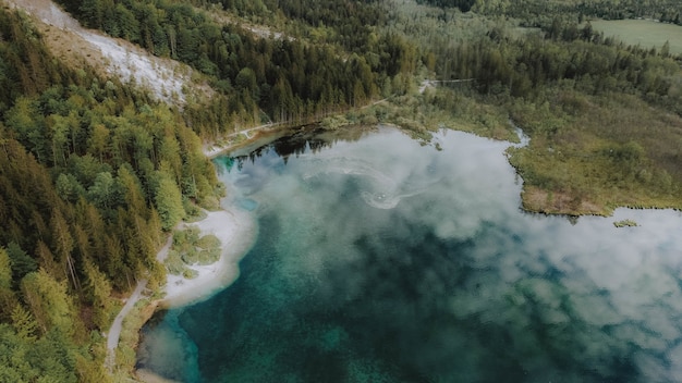 Free photo bird's eye view of a lake surrounded by forests with the cloudy sky reflecting on the water