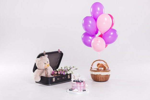 Birthday cake, teddy bear in vintage suitecase and balloons isolated on white background