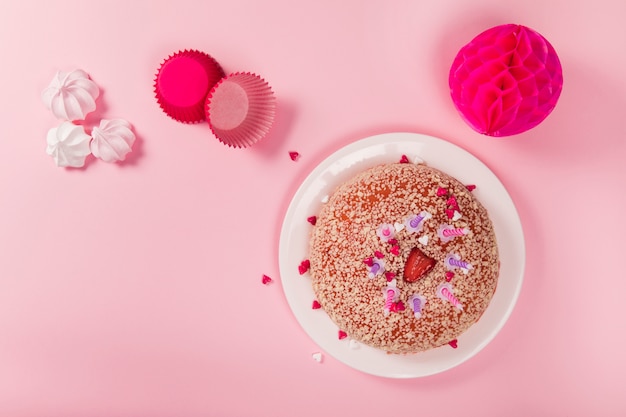 Free photo birthday cake with candles; zephyrs; paper cupcake holder and honeycomb pom-pom paper balls on pink backdrop