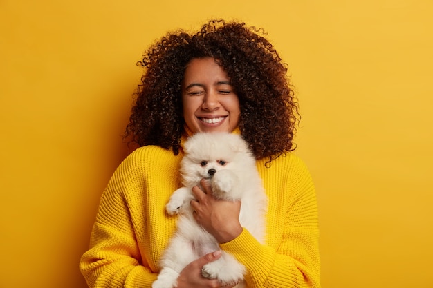 Free Photo birthday woman smiles broadly, gets lovely pet as present, dreams about having spitz long time, wears yellow jumper, stands indoor