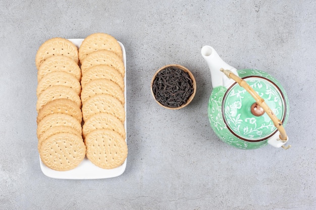 Free photo biscuits lined up on a platter with a teapot and a small bowl of tea leaves on marble surface