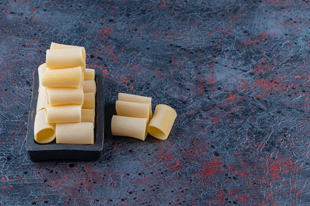 A black board of raw cannelloni pasta on a dark background. 