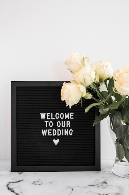 Free photo black board with welcome to our wedding message and rose vase on marble table top