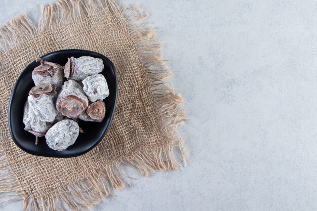 Black bowl of dried persimmon fruits on marble background.