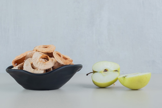 Free photo a black bowl full of dried apple fruit with slices of fresh apple .