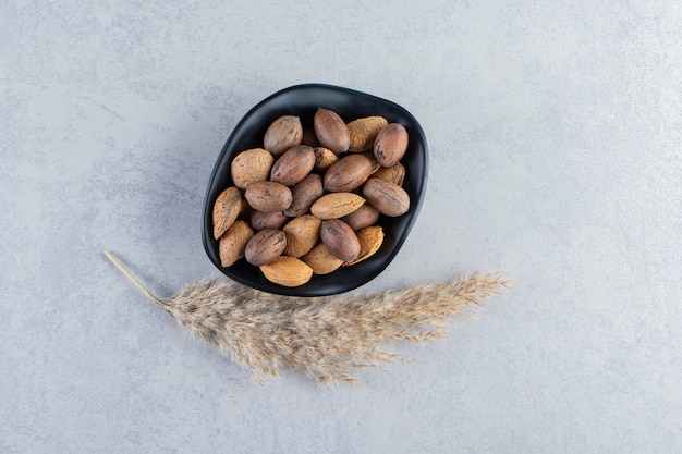 Black bowl full of shelled almonds and walnuts on stone background.