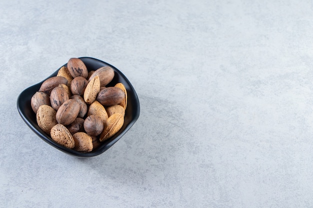 Free Photo black bowl full of shelled almonds and walnuts on stone.