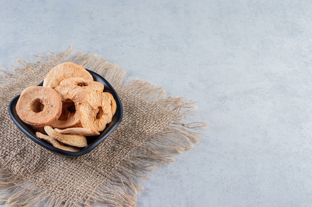 Black bowl of healthy dried apple rings on stone background