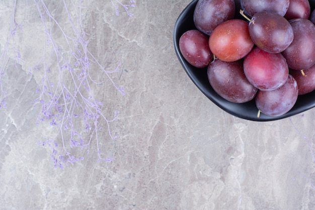 Free photo black bowl of plums on stone background.