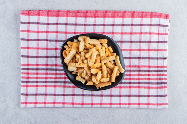 Black bowl of tasty crunchy crackers on stone background.