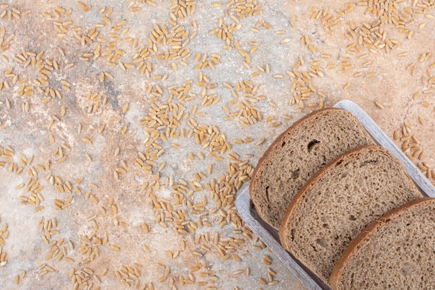 Black bread slices with barley grains on marble surface