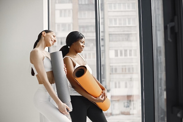 Black and caucasian women standing with rolling mats in studio with big windows