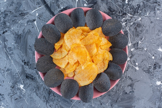 Free photo black chips and potato chips in plate , on the marble surface