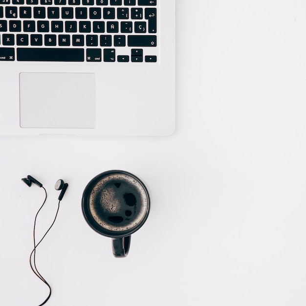 Black coffee cup; earphone and laptop on white desk