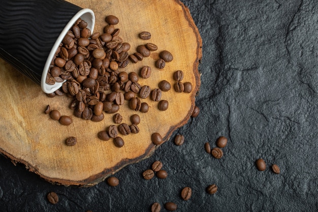 A black cup full of coffee beans on wooden board.