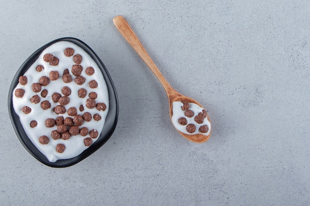 A black deep plate of milk with chocolate cereals and wooden spoon. High quality photo