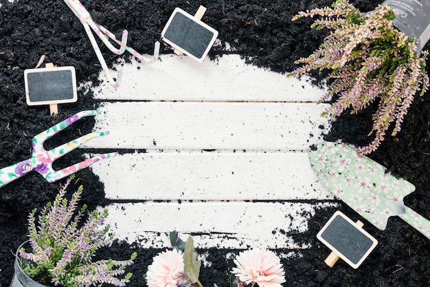 Free photo black dirt; potted plant; flowers; blank chalkboard; and gardening tools over wooden desk