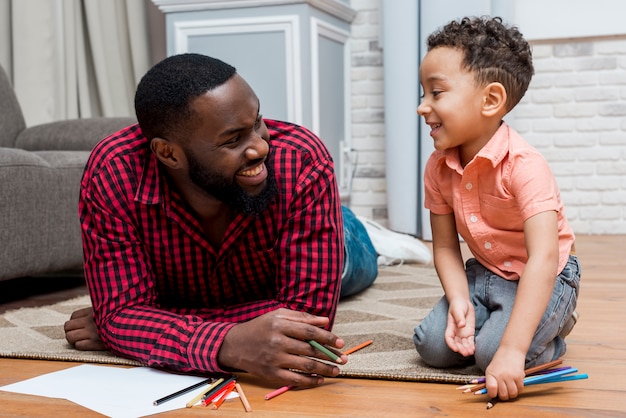 Black father and son with pencils on floor 