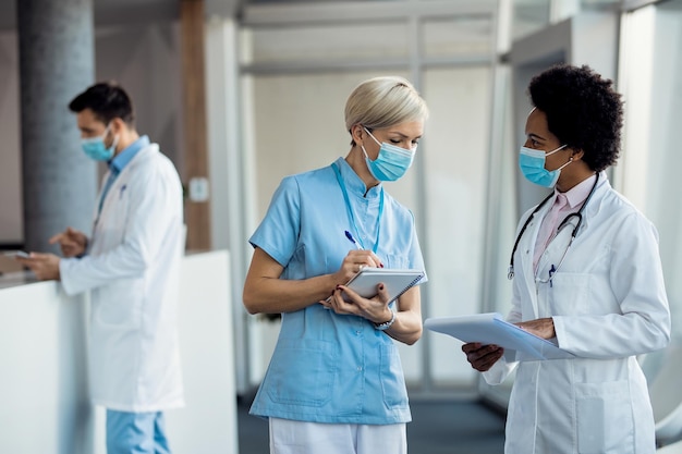 Free Photo black female doctor and nurse with face masks communicating at hospital hallway