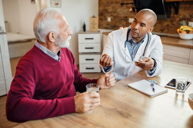 Black general practitioner giving pill to a senior man during home visit