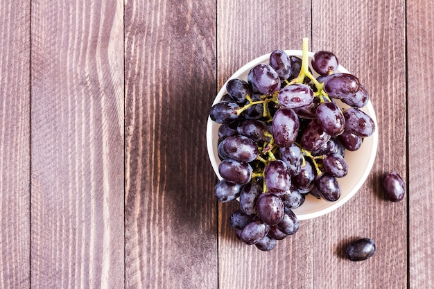 Black grape branch in bowl on dark wood