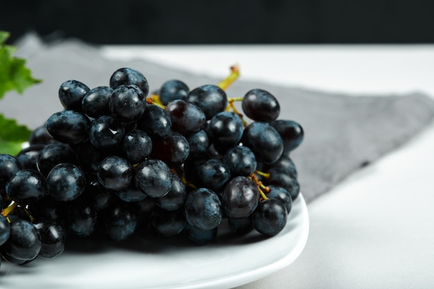 Black grape with leaf on white plate with grey tablecloth. High quality photo