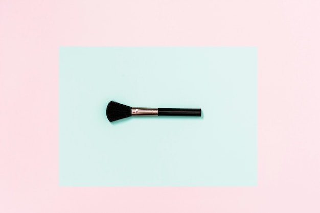 Black makeup brush on teal and pink background