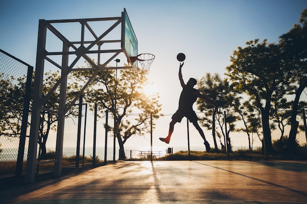 Black man doing sports, playing basketball on sunrise, jumping silhouette