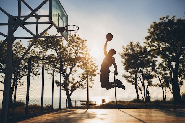 Black man doing sports, playing basketball on sunrise, jumping silhouette