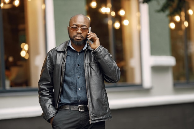 Black man standing on a street in a city. Man wearing sunglasses and a leather jacket