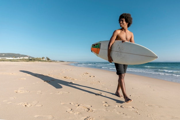 Black man walking along beach with surfboard