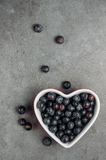 Black olives in a heart shaped bowl on a gray background. top view.