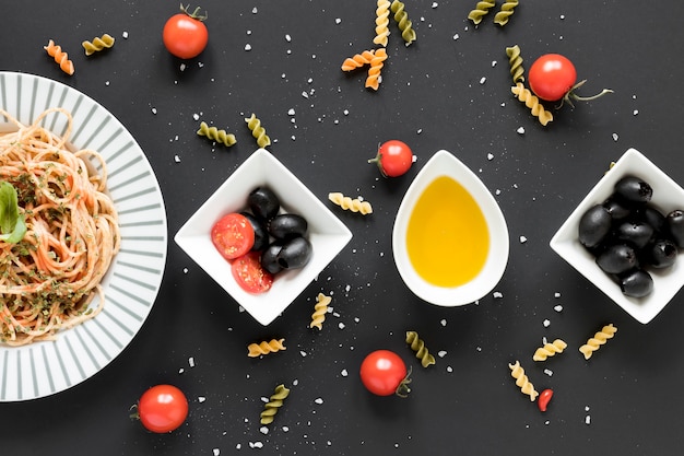 Free photo black olives; oil; cherry tomato and tasty spaghetti pasta arranged over black backdrop