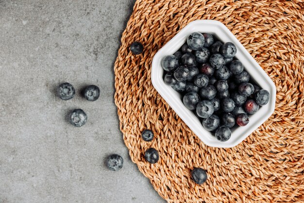 Black olives in a square bowl top view on a rattan trivet and gray background