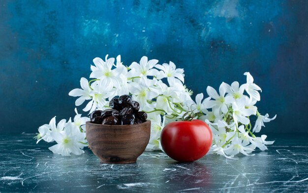 Black olives in a wooden cup with a tomato aside.