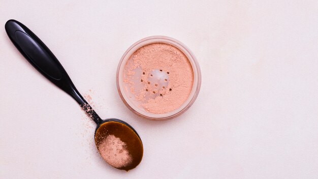 Black oval brush and face powder on pink background