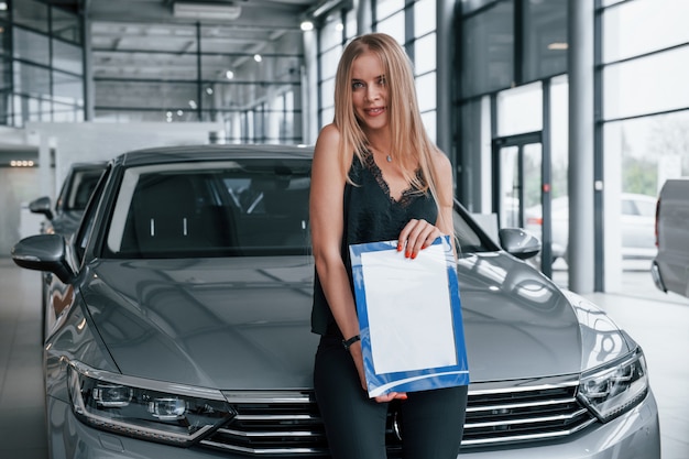 Free photo in black pants. girl and modern car in the salon. at daytime indoors. buying new vehicle