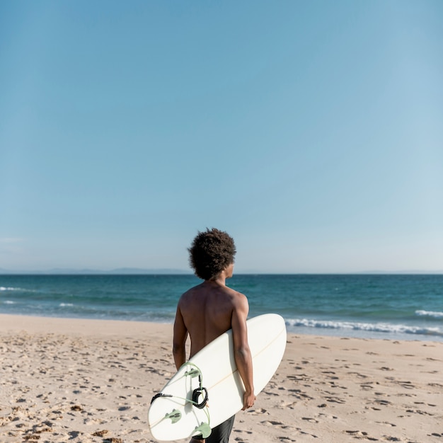 Black pensive man with surfboard looking away